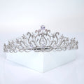 A silver tiara with a large central diamond and smaller diamonds surrounding it, placed on a white surface.