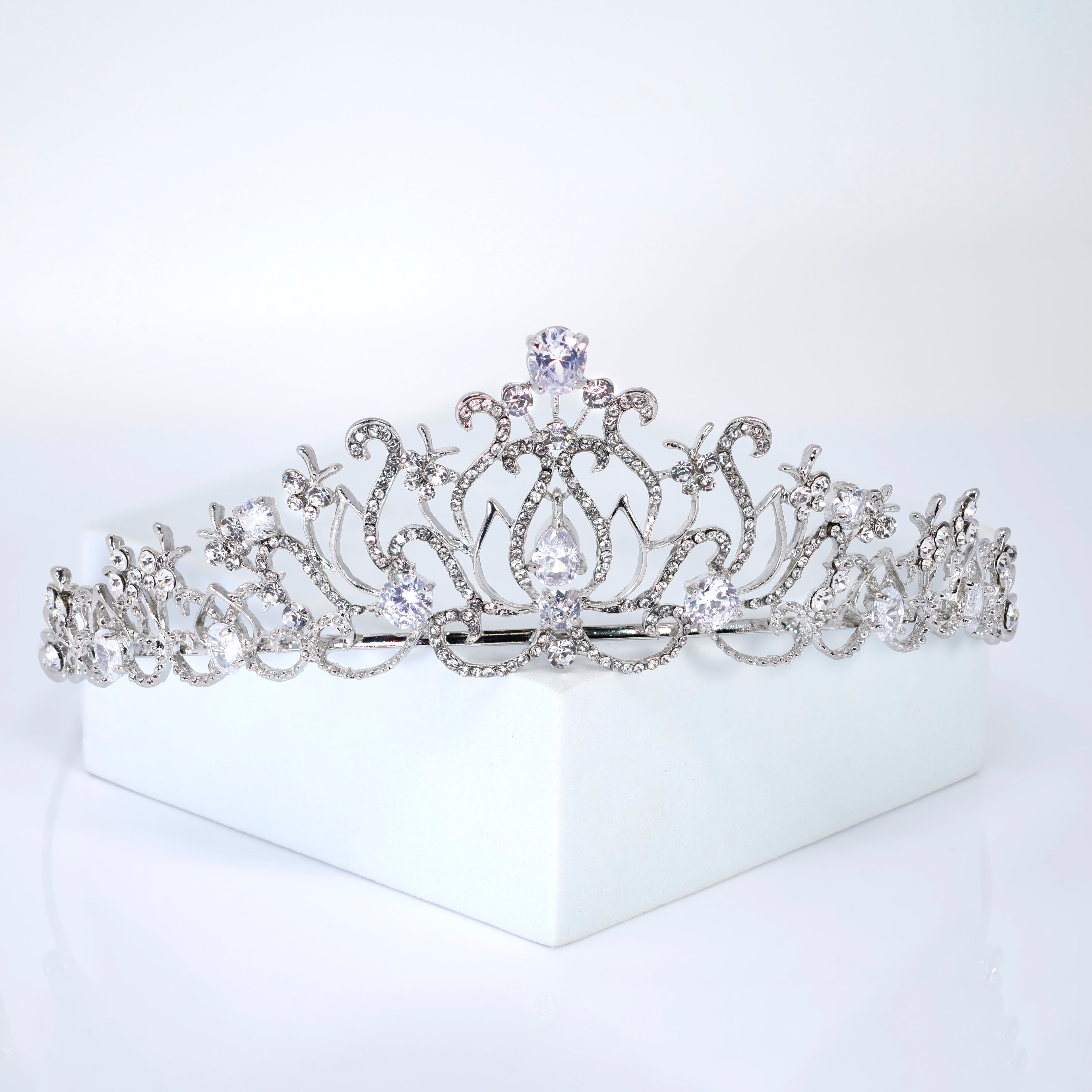 A silver tiara with a large central diamond and smaller diamonds surrounding it, placed on a white surface.