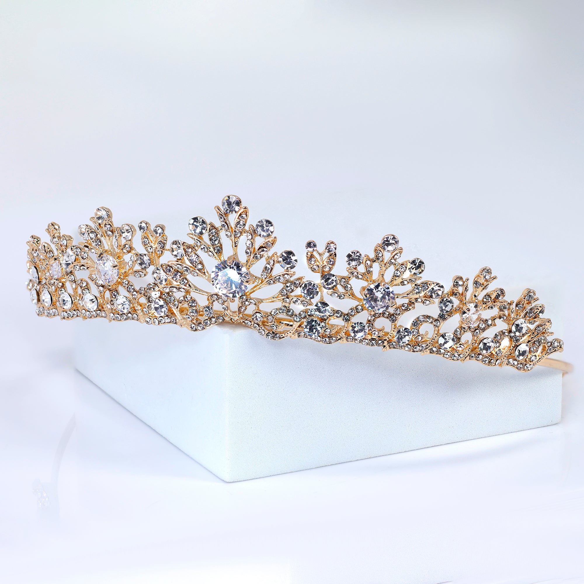 A gold tiara adorned with numerous sparkling diamonds rests on a white surface.