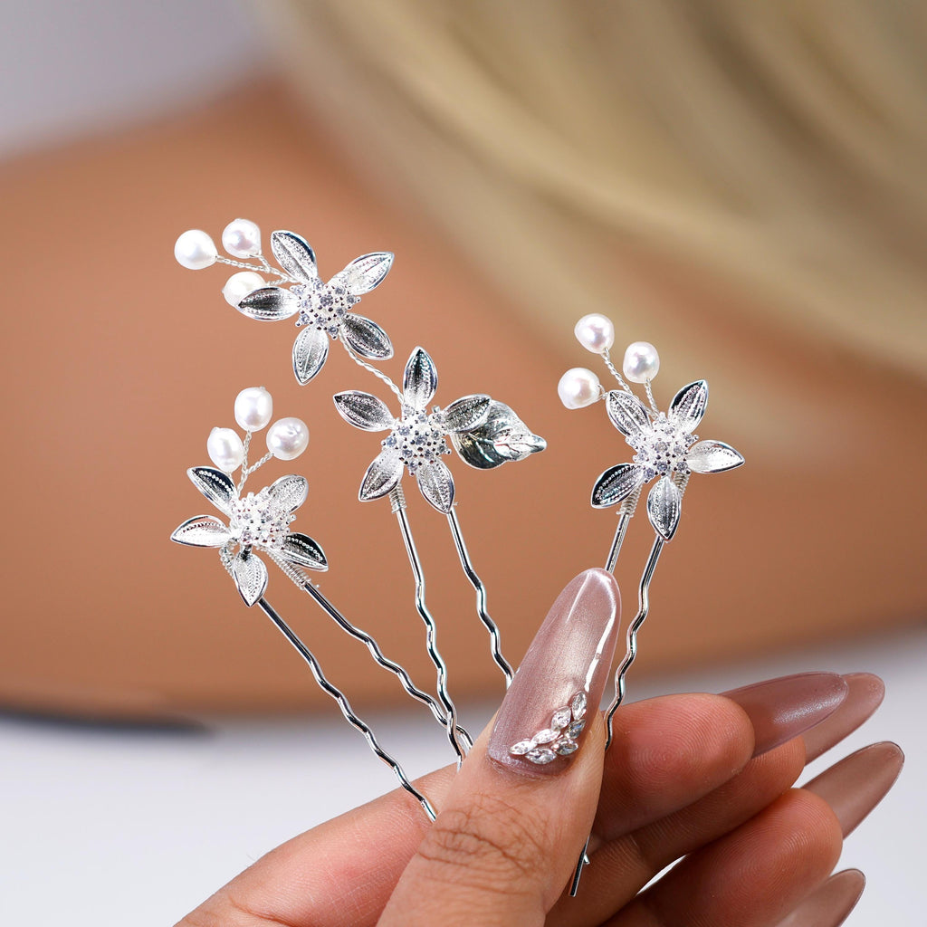 A hand holding a collection of silver hair clips adorned with small white flowers and leaves.