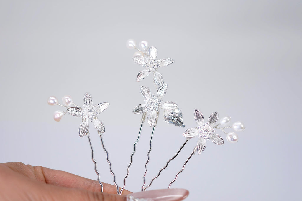 A hand holding a collection of silver hair pins adorned with small white flowers and pearls.
