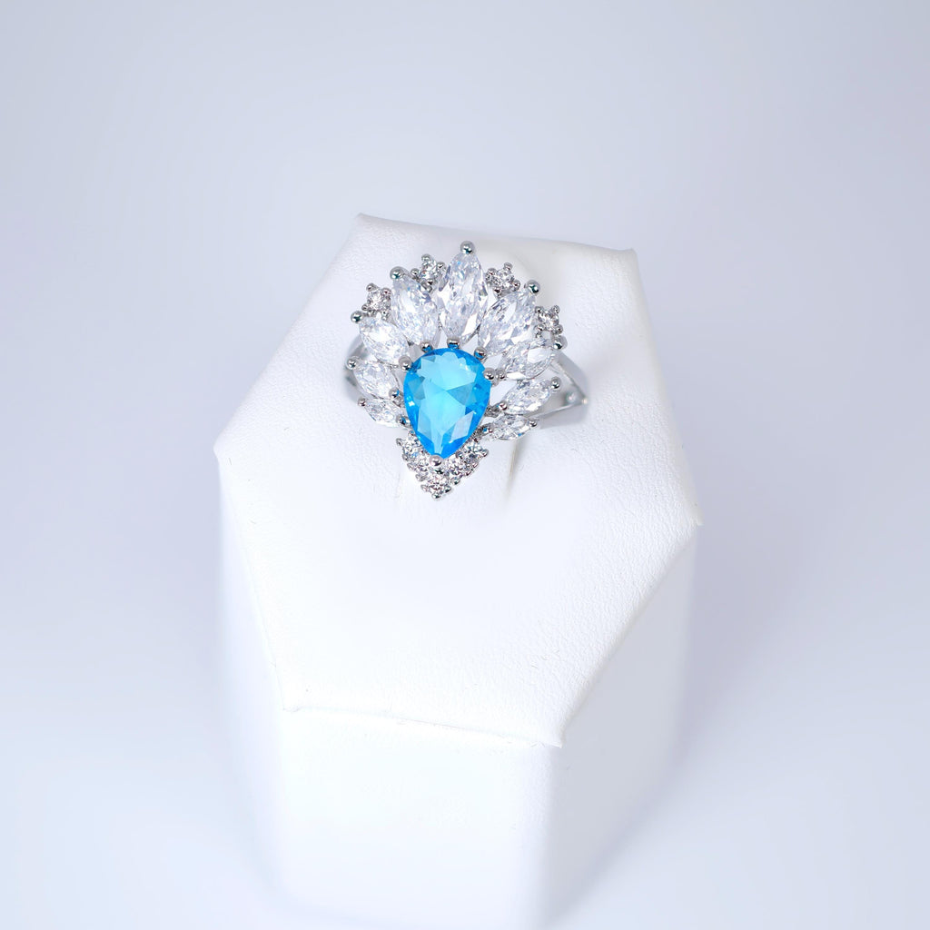 A white jewelry box containing a ring with a blue gemstone.