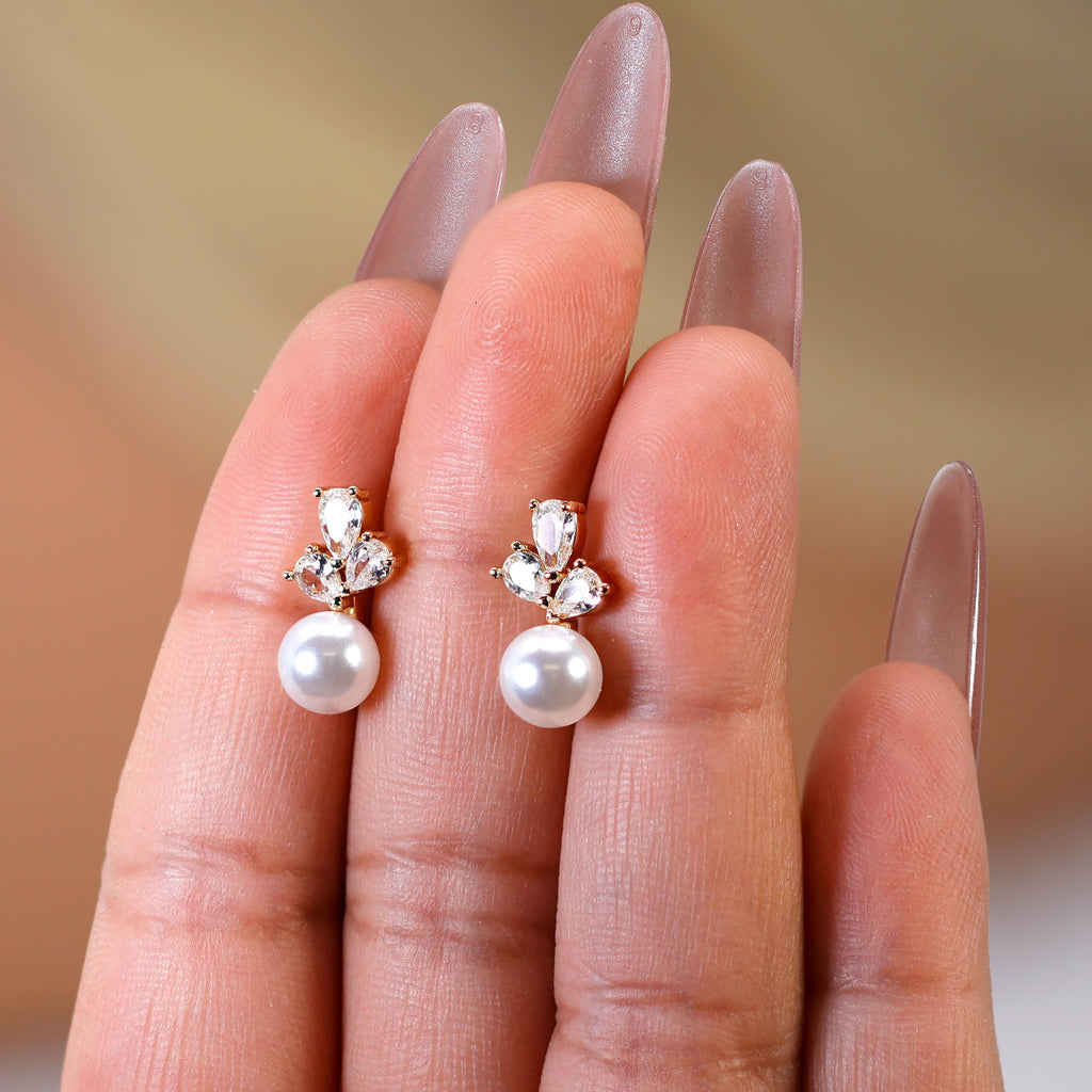 A close-up of a person's hand wearing a pair of pearl drop earrings with gemstone accents.