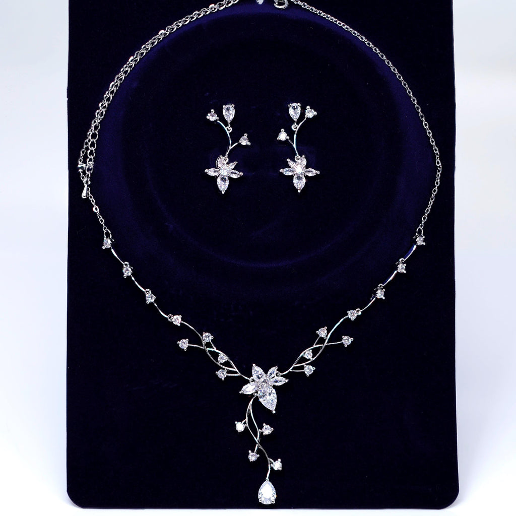 A necklace and earrings set made of white diamonds and silver, displayed on a dark blue velvet background.