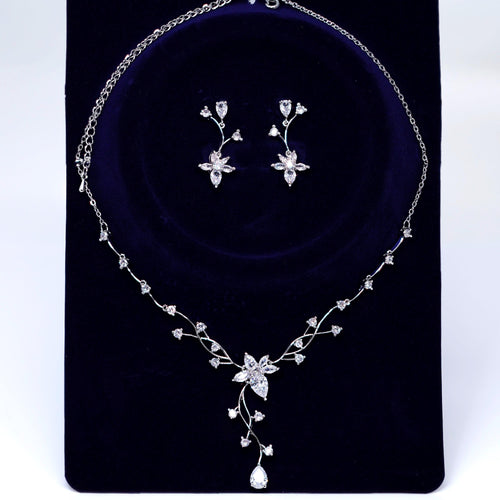 A necklace and earrings set made of white diamonds and silver, displayed on a dark blue velvet background.