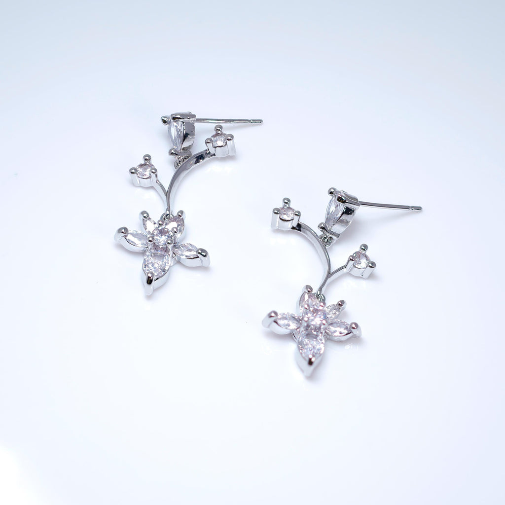 A pair of silver earrings with small, clear gemstones or crystals, resembling a flower or plant design.