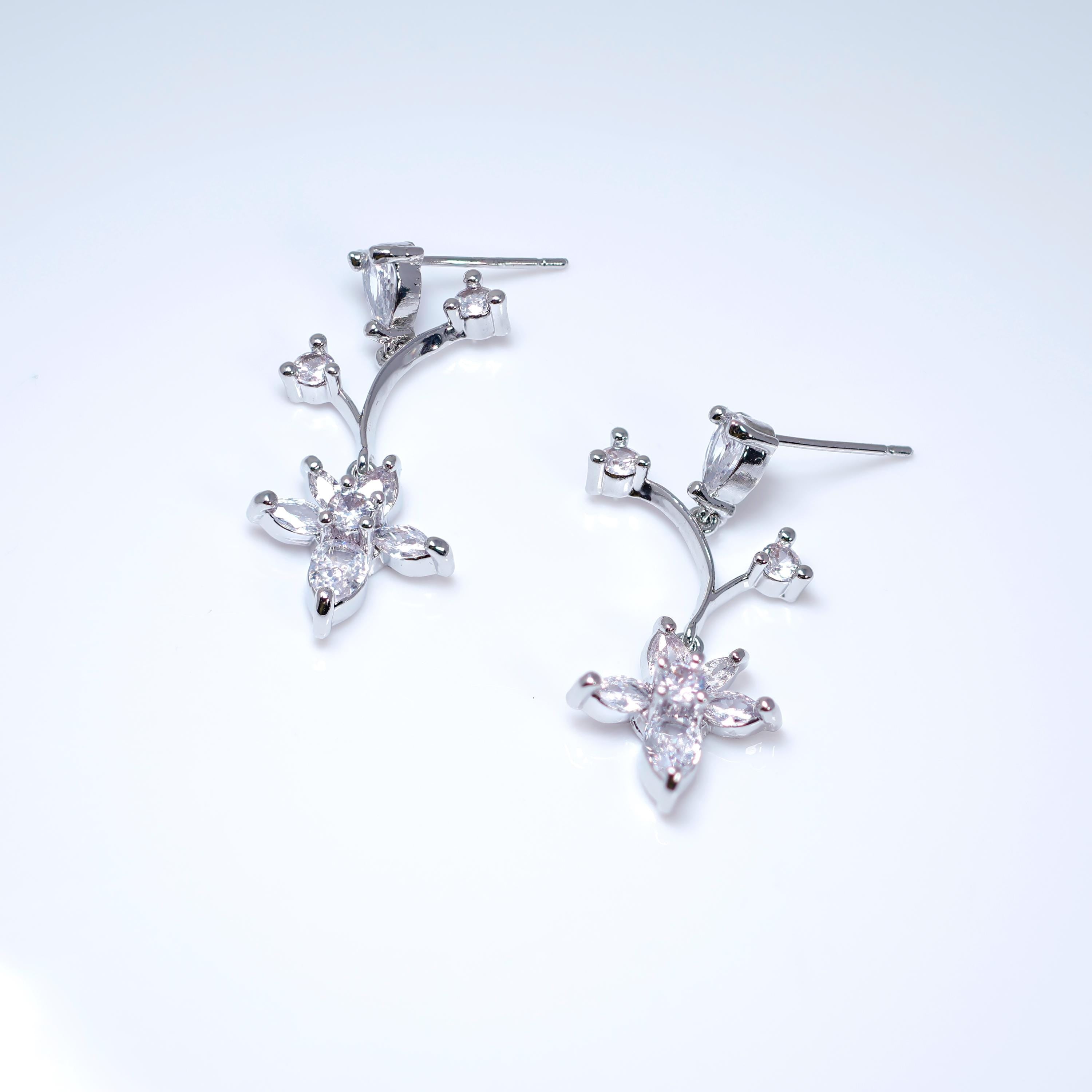A pair of silver earrings with small, clear gemstones or crystals, resembling a flower or plant design.