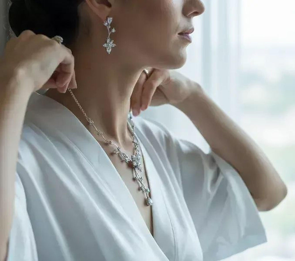 A woman wearing a white robe and a necklace with a large, ornate pendant is adjusting her necklace.