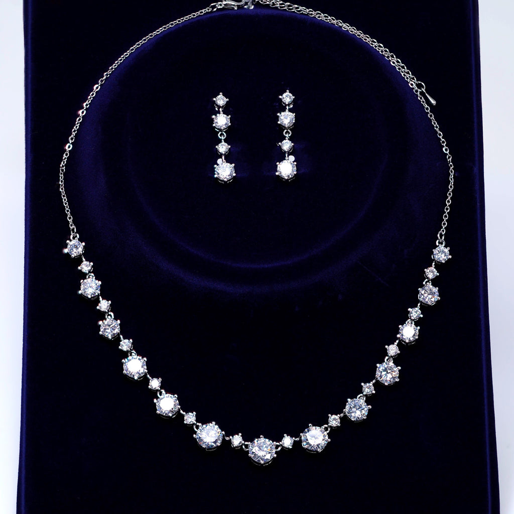 A necklace and earrings set made of white diamonds on a dark blue velvet background.