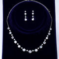 A necklace and earrings set made of white diamonds on a dark blue velvet background.