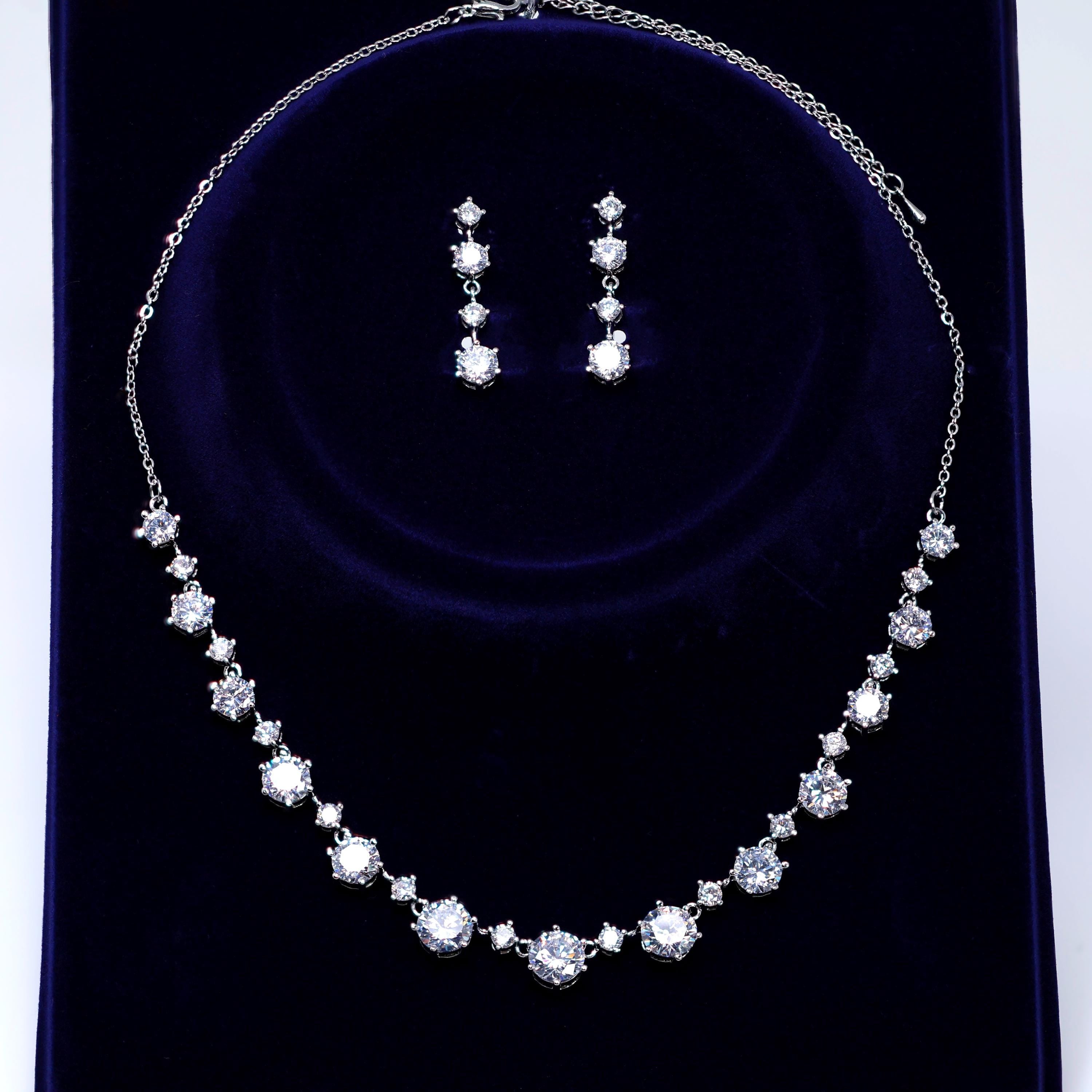 A necklace and earrings set made of white diamonds on a dark blue velvet background.