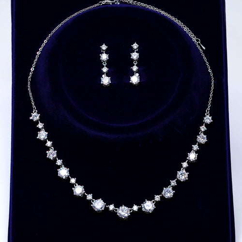 A necklace and earrings set made of white diamonds on a dark blue velvet background.