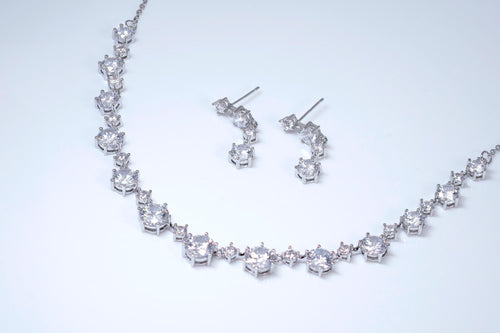 A necklace and earrings made of sparkling diamonds are displayed against a white background.