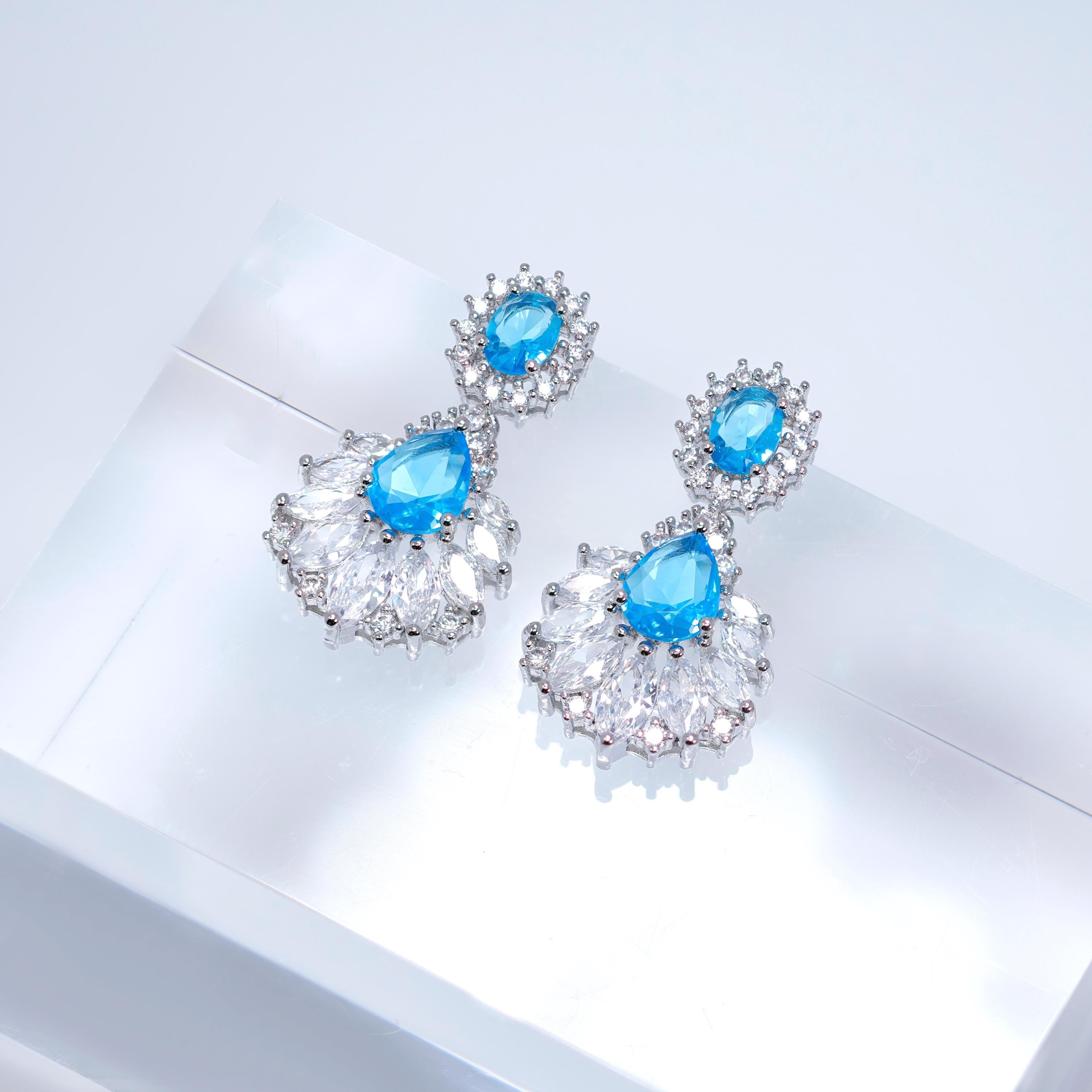 A pair of elegant earrings with blue gemstones and intricate silver designs, displayed on a white surface.