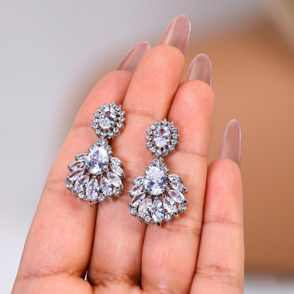 A close-up of a person's hand holding a pair of elegant diamond earrings.