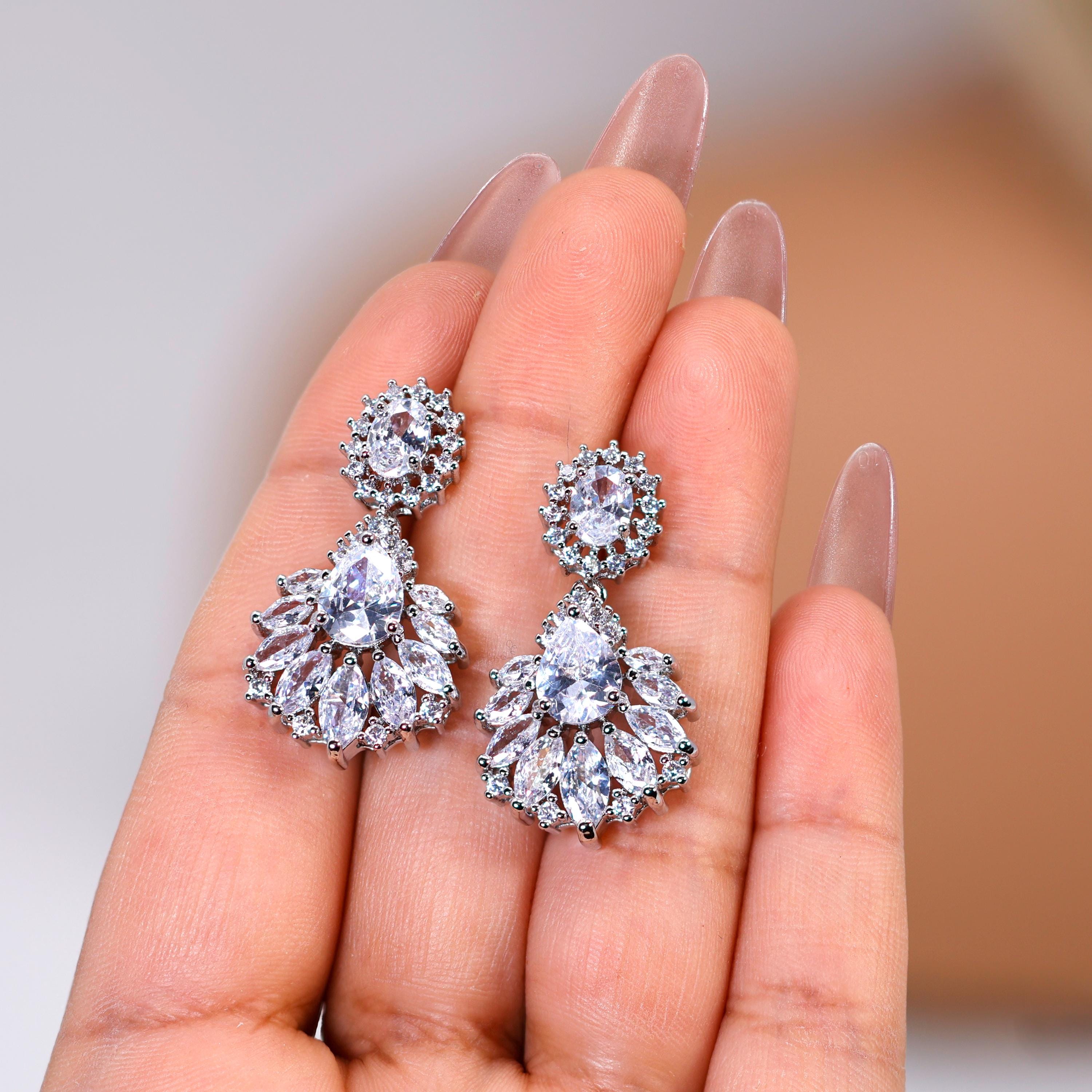 A close-up of a person's hand holding a pair of elegant diamond earrings.