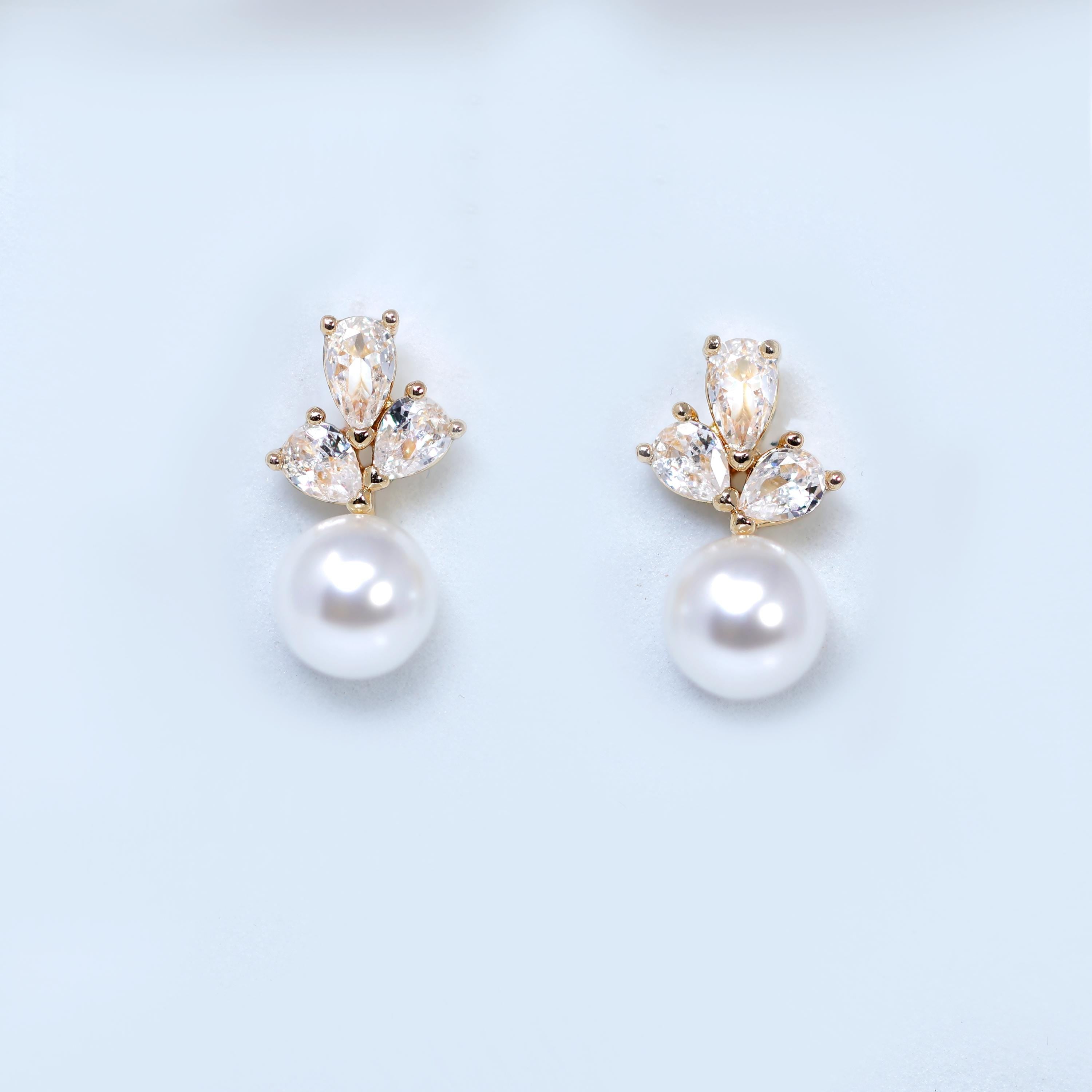 A pair of elegant earrings with a pearl and a cluster of small, clear gemstones.
