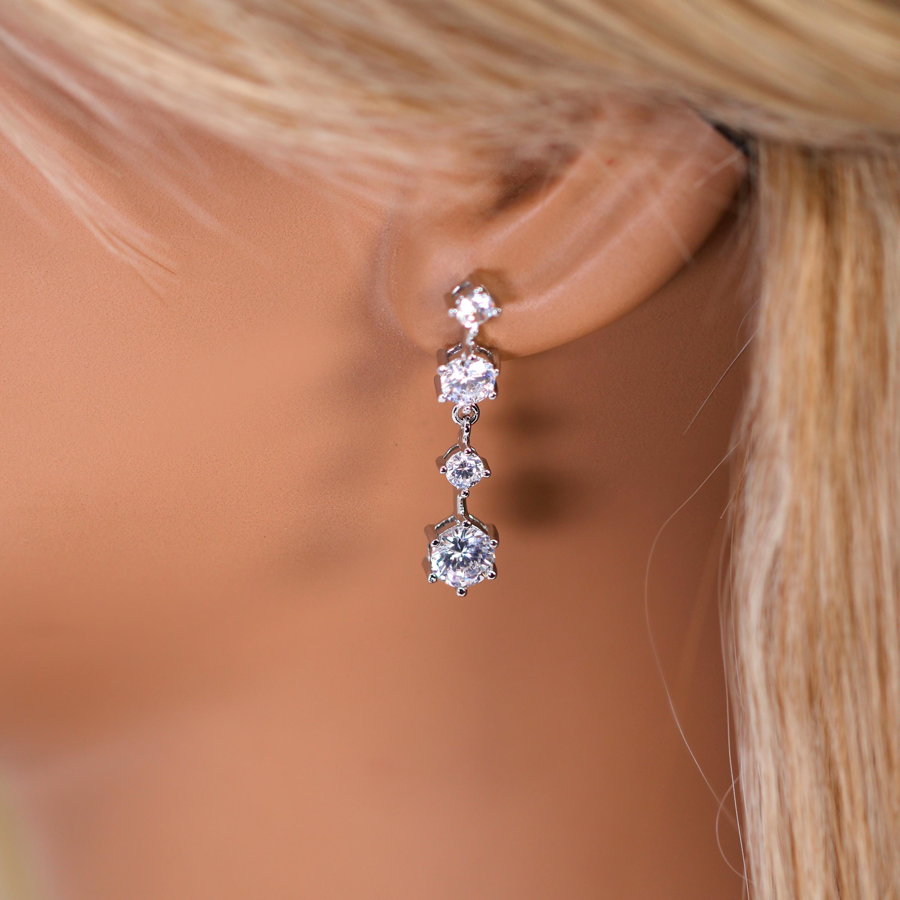 A close-up view of a person's ear adorned with a delicate, dangling earring featuring a row of small, clear gemstones.