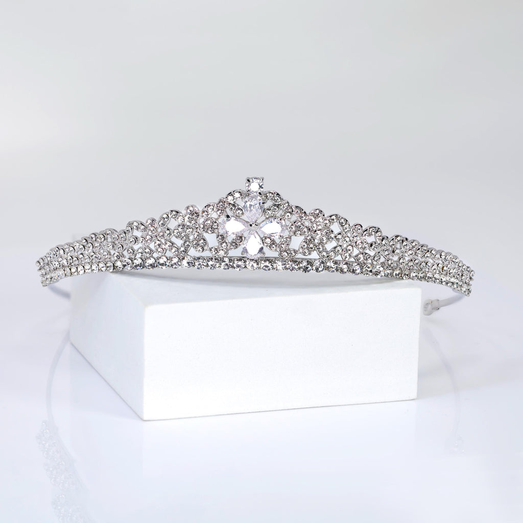 A silver tiara with a large crystal center stone is displayed on a white surface.