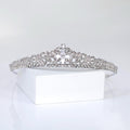 A silver tiara with a large crystal center stone is displayed on a white surface.